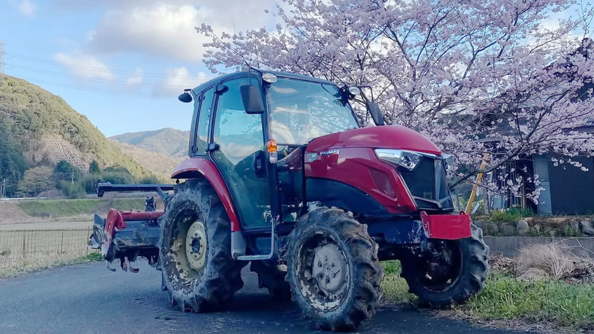有限会社グリンファーム旭のトラクターの写真。桜と一緒に撮影している。